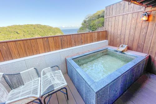 a hot tub on a balcony with two chairs at 鵜原館 -Ubarakan- in Katsuura