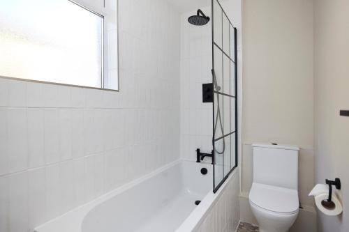 a white bathroom with a toilet and a window at The Leyton Midland Crib - Cozy 2BDR Flat with Study Room + Garden in London