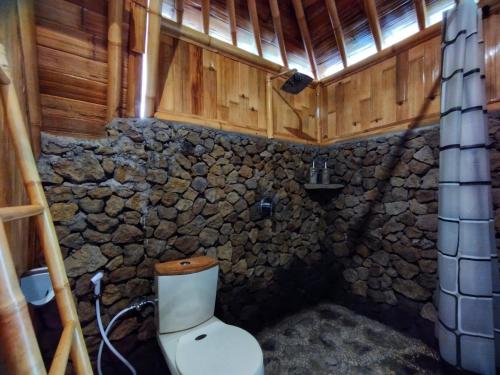 a bathroom with a toilet and a stone wall at Aksha Riverside Ubud in Tampaksiring