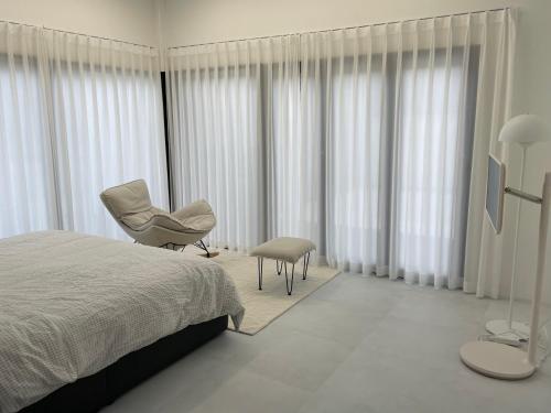 1 dormitorio con cama, silla y cortinas en 신규오픈, 프라이빗 독채 풀빌라 펜션, 스테이티모가, en Muju