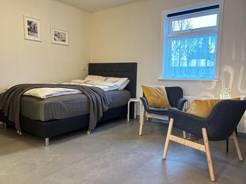 a bedroom with a bed and two chairs and a window at Cozy Bungalow in Reykjavík