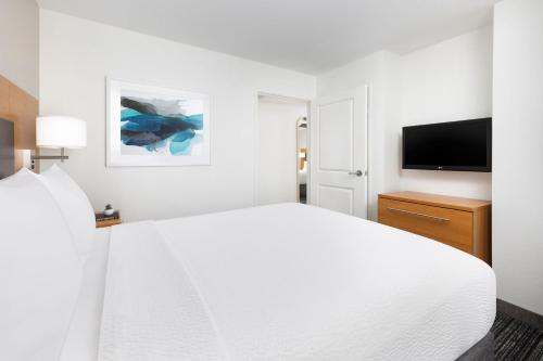 a white bedroom with a bed and a flat screen tv at TownePlace Suites by Marriott Roswell in Roswell