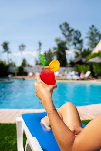 a woman is holding a drink in front of a pool at Hotel Onix in Viseu