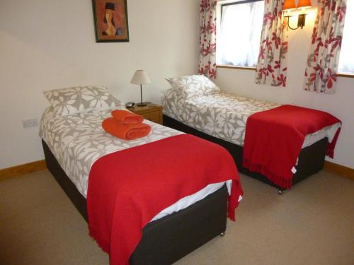 a bedroom with two beds with red sheets and a window at Withersdale Cross Cottages in Mendham