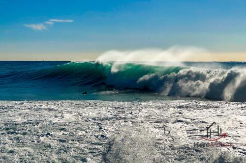 a surfer riding a large wave on a beach at [Penthouse with Terrace] • Sea 5Min • Trains 4Min in Varazze