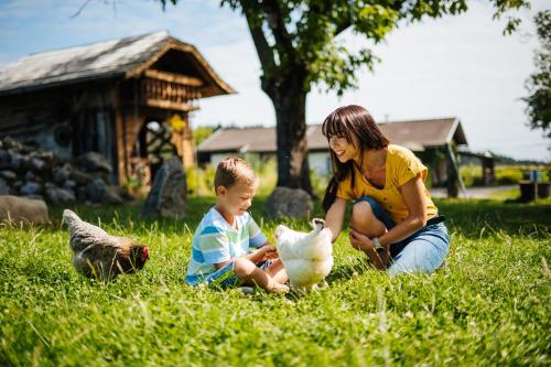 una mujer y un niño sentados en la hierba con un pollo en Erlebnisbauernhof Tschom, en Sankt Kanzian