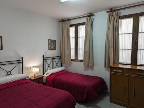 a bedroom with two beds with red sheets and windows at Pensión Ciudad Navarro Ramos in Granada