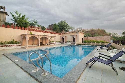 a swimming pool with two chairs next to a house at Fort Beejwar Chauhan by AAYAMs Neemrana in Shāhjahānpur