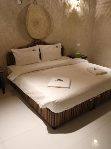 Una cama con sábanas blancas y un sombrero. en Canyon Rest House Jabal Shams en Al Ḩamrāʼ