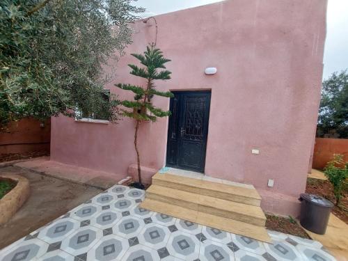 une maison rose avec une porte noire et un arbre dans l'établissement Traveler's house, à Jerash