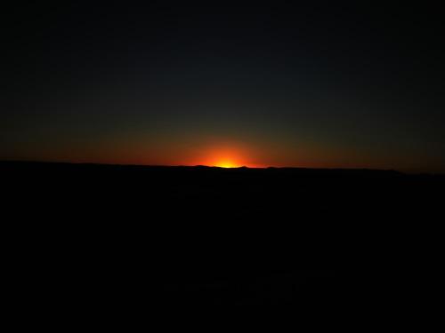 a sunset in a field with the sun in the background at Holiday Desert Camp in Merzouga