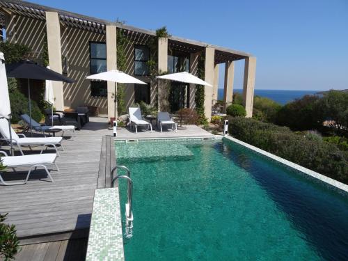 a swimming pool with chairs and umbrellas next to a building at Villa Libecciu in Sainte-Lucie de Porto-Vecchio