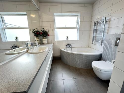 een badkamer met 2 wastafels, een bad en een toilet bij Spacious and family friendly apartment in Kópavogur in Reykjavík