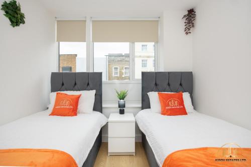 2 bedden met oranje kussens in een kamer met een raam bij Hephaestus Apartment - The Craftsman of Town in Southampton