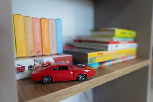 a red toy car sitting on a shelf with books at 'Just like home' Apartment - with Private Parking Place in Galaţi