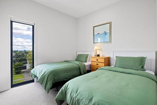 two beds in a white room with a window at Seaside Serenity at Bask Retreats in Mount Maunganui