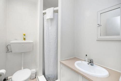 La salle de bains blanche est pourvue de toilettes et d'un lavabo. dans l'établissement The Sands Motel, à Tutukaka