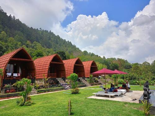 a group of huts with people sitting under an umbrella at D’Taman cabin Kintamani in Kubupenlokan
