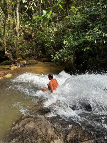 a man is sitting in a stream of water at Casa de campo com cachoeira no quintal in Gaspar