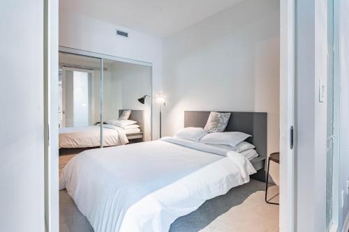 a white bedroom with two beds and a mirror at Spacious Lakefront Condo+Parking+Pool+Gym+Patio in Toronto