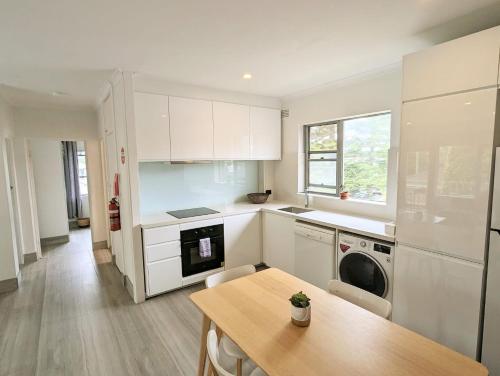 a kitchen with white cabinets and a table and a washer at Lotus Stay Manly - Apartment 29E in Sydney