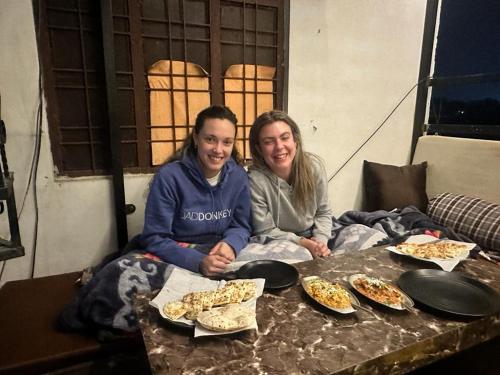 zwei Frauen sitzen an einem Tisch mit Pizza-Scheiben in der Unterkunft Hotel Zoola Palace in Pushkar