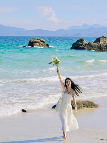 a woman in a white dress holding a bouquet on a beach at Shenzhen Semporna Beach Sea View B & B - 深圳较场尾仙本那沙滩海景民宿 in Shenzhen