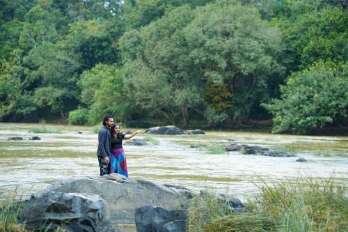 a man and woman standing on a rock in a river at Kuruva Island Resort And Spa - By KABINI BREEZE in Mananthavady