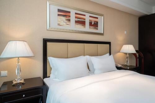 a bedroom with a large white bed with two lamps at Oriental Ginza Hotel Shenzhen in Shenzhen