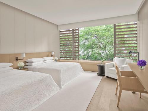a white bedroom with two beds and a window at The Singapore EDITION in Singapore