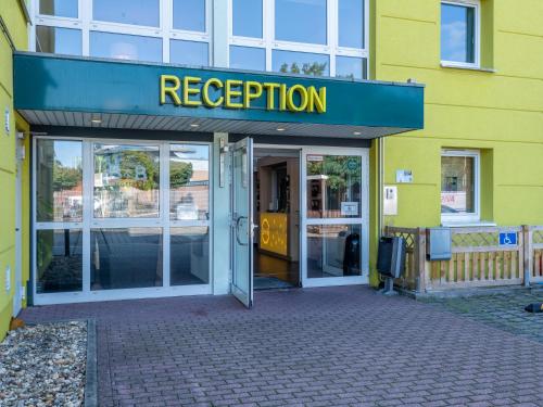 een geel gebouw met een bord dat de receptie leest bij B&B HOTEL Aachen-Würselen in Würselen