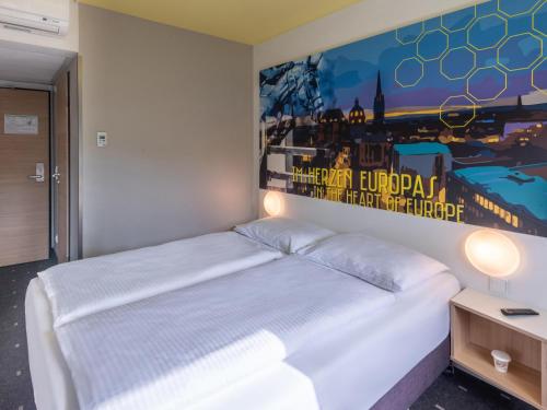 um quarto com uma cama branca e uma pintura na parede em B&B HOTEL Aachen-Würselen em Würselen