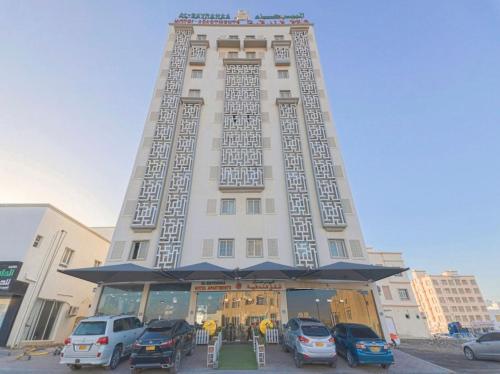 a tall building with cars parked in front of it at Albayrahaa Hotel in Seeb