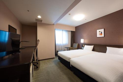 a hotel room with two beds and a flat screen tv at Smile Hotel Premium Kanazawa Higashiguchiekimae in Kanazawa