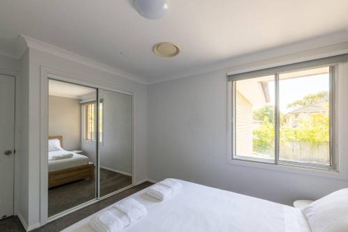 a white bedroom with a bed and a window at The Spotted Gum Northern Beaches in Warriewood