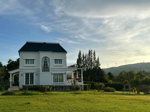 a white house with a black roof on a green field at Misty English Cottage in Ban Non Na Yao
