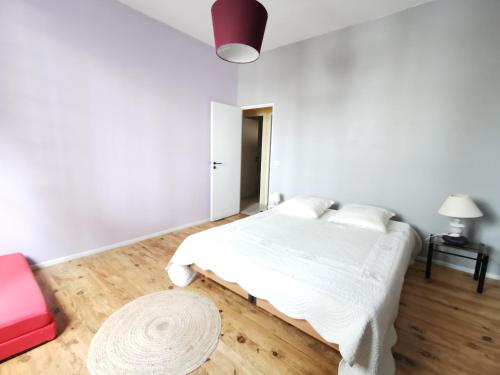 a white bedroom with a bed and a red chair at Logement vue Garonne in Bordeaux