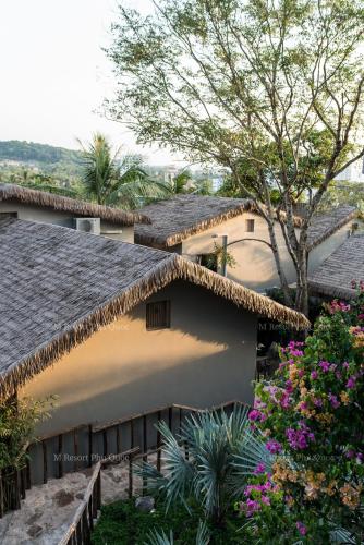 a house with a thatched roof and some flowers at M Village Phu Quoc in Phu Quoc
