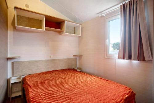 una camera da letto con un letto con un piumone arancione e una finestra di Bungalow T2 i i i - 15 Min Nazaré a Pataias
