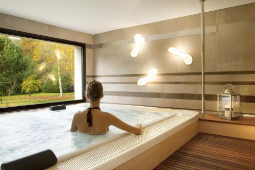 a woman sitting in a bath tub with a window at L'Aubinière Hôtel Restaurant & Spa in Saint-Ouen-les-Vignes