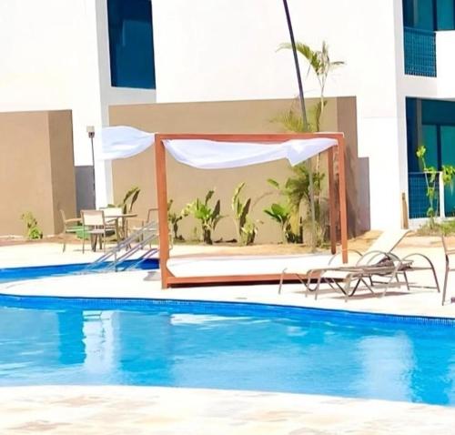 a hotel swimming pool with a bed and umbrella at Makia Flat Muro Alto in Porto De Galinhas