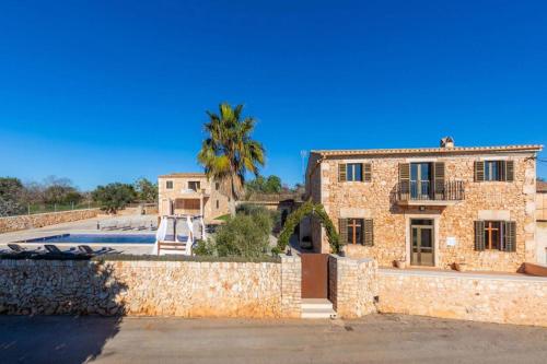 a stone house with a palm tree behind a wall at Villa S`Alzina by Slow Villas in Santanyi