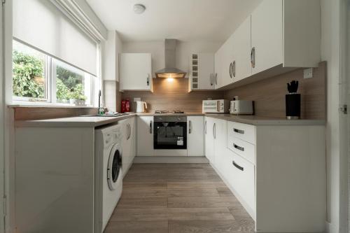 Una cocina con gabinetes blancos y lavadora y secadora. en Glenisla House, en Glasgow