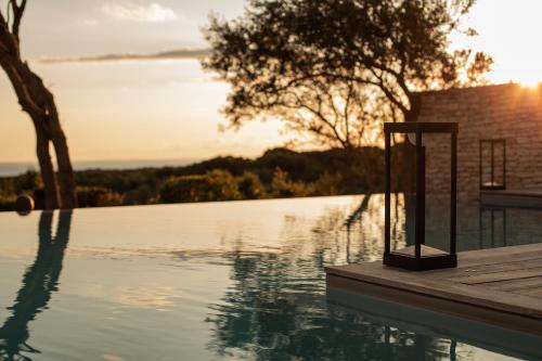 a swimming pool with the sun setting over the water at Hôtel Cala di Greco in Bonifacio