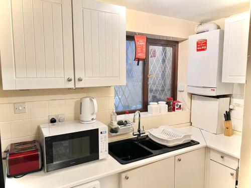 a white kitchen with a microwave and a sink at Cosy 2 bedroom Detached House in Central London in London