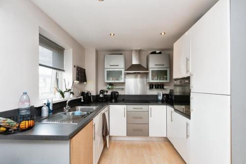 a kitchen with white cabinets and a black counter top at Travaal.©om - 2 Bedroom Apartment - Basingstoke in Basingstoke