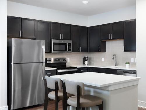 a kitchen with black cabinets and a stainless steel refrigerator at AVE Las Colinas - Short Stay Furnished Apartment in Irving