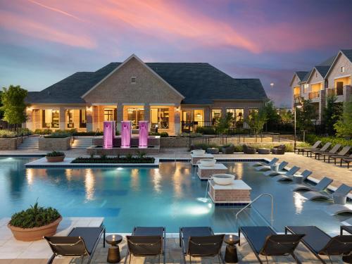 a pool with chairs and tables in front of a house at AVE Las Colinas - Short Stay Furnished Apartment in Irving