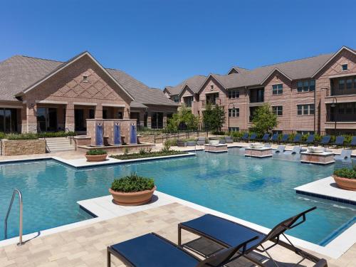 a swimming pool at a resort with chairs and a building at AVE Las Colinas - Short Stay Furnished Apartment in Irving
