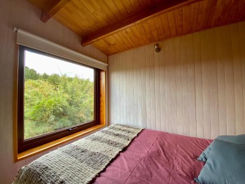 a bed in a room with a window at Tinyhouse Pichi I - vida lenta en Patagonia Costa in Calbuco